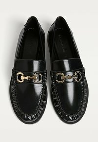 Schwarze Lederschuhe mit glänzender Oberfläche, runder Spitze, elastischen Kanten und goldenen Designdetails mit einer Kettenoptik.