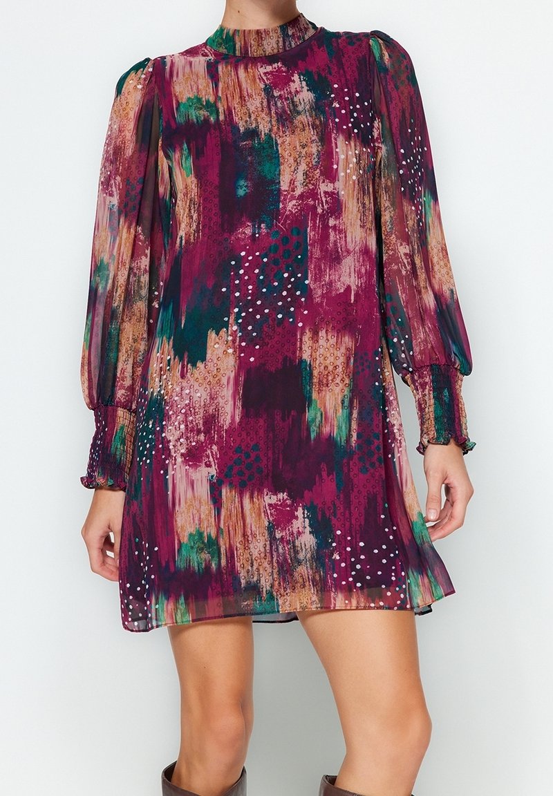 Robe à manches courtes, multicolore dans des tons de violet, vert et beige, avec un motif texturé et des poignets froncés. Le tissu est transparent et fluide.