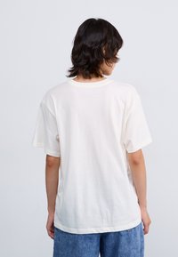 Hvit bomulls t-skjorte med korte ermer, rund hals og avslappet passform. Stoffet virker mykt med en jevn tekstur.