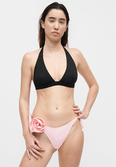 Γυναίκα που φοράει μαύρο τοπ μπικίνι με λαιμόκοψη halter και ανοιχτό ροζ μπικίνι κάτω μέρος με ένα μεγάλο ροζ υφασμάτινο λουλούδι στη αριστερή πλευρά.