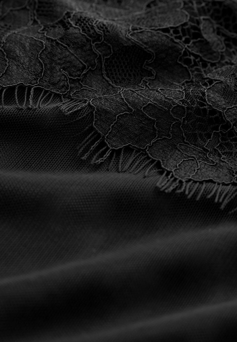 Schwarzer Stoff mit einer floralen Spitzenüberlagerung und kunstvollen Mustern. Die Kanten zeigen eine fransige Ausarbeitung, die die Textur verstärkt.