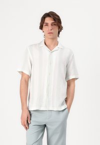 Camicia a maniche corte, con bottoni, di un colore crema chiaro con sottili strisce verticali in colori pastello. Vestibilità rilassata con collo da campeggio e tessuto texturizzato.