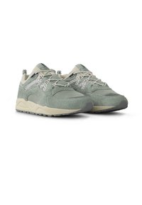 Zapatillas deportivas verdes claras con una mezcla de materiales de ante y malla, con una parte superior texturizada, suela de color blanco hueso contrastante y diseño con cordones.