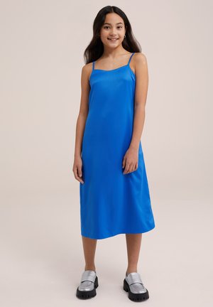 Blue satin slip dress with thin straps, knee-length, smooth texture. Paired with silver loafers with chunky black soles.