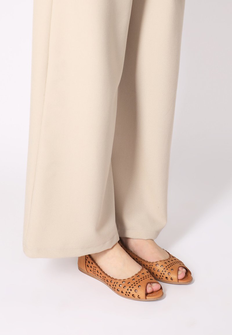 Tan Peep-Toe-Ballerinas mit ausgeschnittenem Design, aus Leder gefertigt. Mit einer glatten Oberfläche und runder Zehenpartie. Getragen mit beigen weit geschnittenen Hosen.