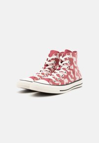 Des baskets montantes en tissu rose avec un motif abstrait blanc. Elles sont dotées de lacets blancs, d'un capuchon en caoutchouc à l'avant et d'une bande noire le long de la semelle.
