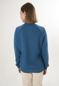 Niebieski bawełniany sweatshirt z długimi rękawami, okrągłym dekoltem i krojem raglanowym. Charakteryzuje się gładką teksturą i ściągaczem u dołu.