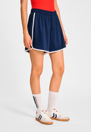 Mörkblå sportshorts med vit kant, resårmidja och lätt tyg, kombinerade med vita crew-strumpor och sneakers i retrostil.