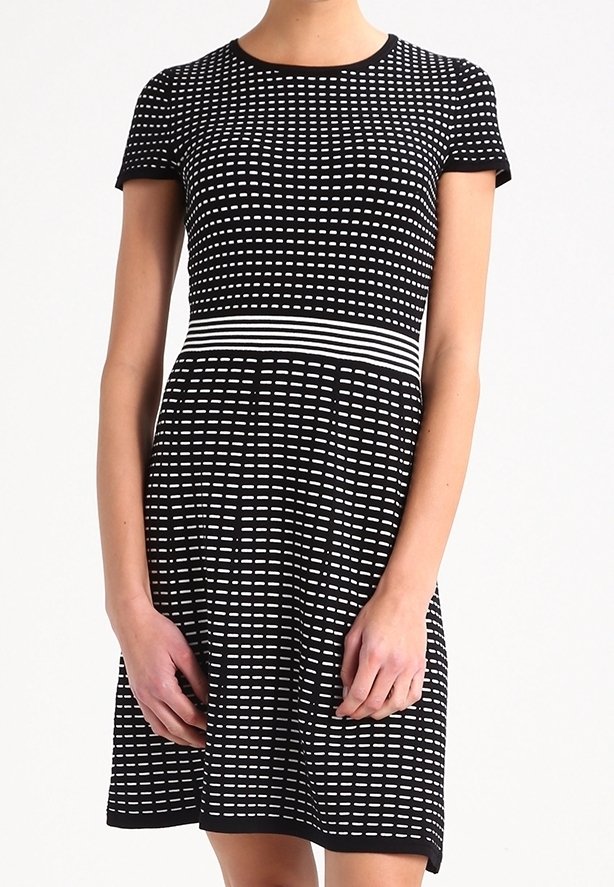 Femme portant une robe noire à manches courtes avec des rayures horizontales blanches en pointillés et une bande rayée blanche à la taille.