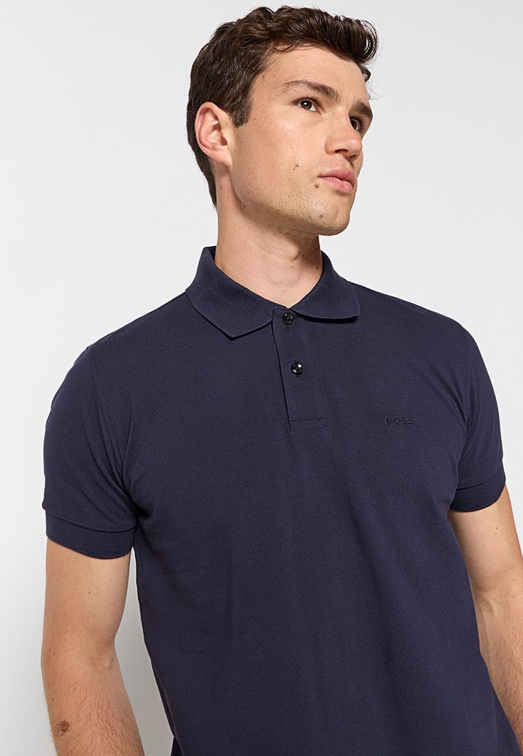 Polo blu navy realizzato in tessuto testurizzato, con colletto classico, patta con due bottoni e un sottile dettaglio del logo sul petto.