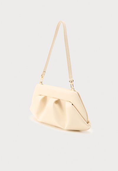 Τσαντάκι ώμου από απαλό δέρμα σε κρεμ απόχρωση με χρυσά μεταλλικά στοιχεία, σχέδιο που μοιάζει με πουγκί και λεπτό αποσπώμενο λουράκι σε ανοιχτό φόντο.