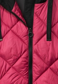 Vadderad jacka i stark rosa med diamantsöm, med en svart dragkedja, textildetaljer och design med ståkrage.