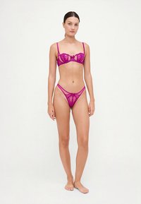 Komplet spodnjega perila iz fuksijastega čipke, ki vključuje modrček z oporo in podrobnostjo v obliki pentlje ter ujemajoče se tangice s tankimi stranskimi pasovi.