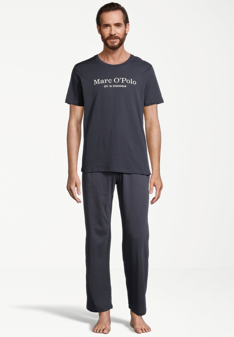Mørkegrå pyjamas sæt med en kortærmet t-shirt med hvid "Marc O'Polo" tekst og matchende lange bukser lavet af blødt stof.