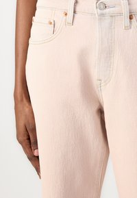 Jeans de mezclilla rosa claro con una superficie texturizada, que presentan costuras en contraste, un diseño de cinco bolsillos y un cierre de botón metálico.