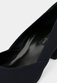 Mornarsko plava ravna cipela sa zaobljenim vrhom, glatkim mat završetkom i teksturiranim crnim uloškom, s minimalističkim dizajnom i niskom blok petom.