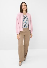 Lichtroze bomberjack, gebloemd top met blauwe en groene tinten, beige wijde broek en taupe flats. Soepele texturen en een ontspannen pasvorm.