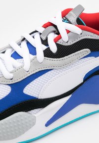 Sneaker z siateczkowym wierzchem w niebieskie, białe, szare i czarne akcenty, grube białe sznurowadła oraz wyściełane czerwone wnętrze. Teksturowana gumowa podeszwa.