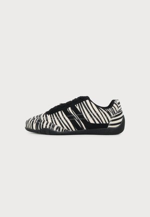 Basket basse avec rayures zèbre noires et blanches, lacets noirs et semelle noire texturée, vue de profil sur fond blanc.