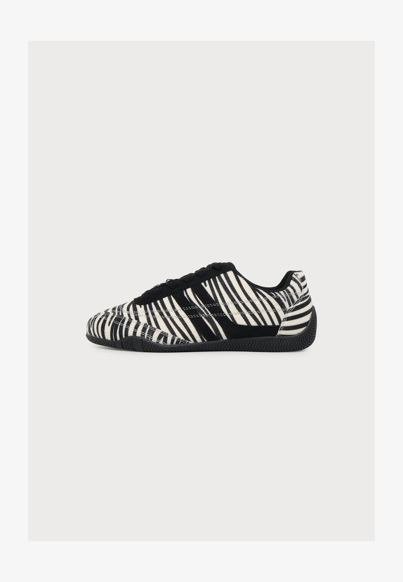 Basket basse avec rayures zèbre noires et blanches, lacets noirs et semelle noire texturée, vue de profil sur fond blanc.