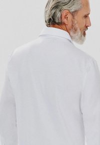 Biała koszula z długim rękawem o klasycznym kołnierzyku, gładkiej fakturze i dopasowanym kroju, widoczna z tyłu, podkreślająca czysty design.