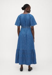 Vestido maxi de denim con mangas cortas, cintura fruncida y dobladillo de volantes en capas. Presenta una textura azul y sutiles detalles de costura.