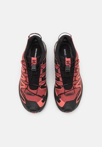 Des chaussures de course rouges et noires avec une tige en tissu texturé, conçues pour le soutien, dotées d'un système de laçage sécurisé et d'accents de marque bien visibles.