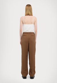 Top bianco a spalline sottili abbinato a pantaloni a gamba larga marroni. I pantaloni presentano una vita elasticizzata e due tasche posteriori; tessuto liscio e strutturato.