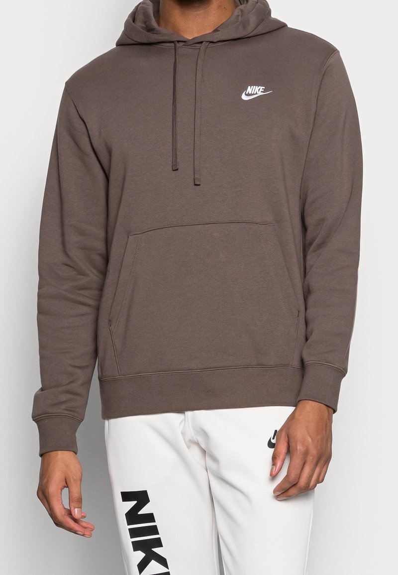 Brązowa bluza z kapturem z kieszenią z przodu, regulowanym sznurkiem na kapturem oraz białym logo Nike na piersi. Miękka tkanina i luźny krój.