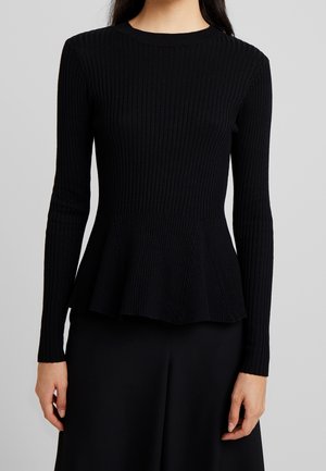 Zwart geribd top met lange mouwen, aangesloten lijfje en uitlopende peplumzoom, gedragen door een persoon met lang donker haar.