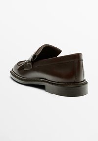 Dark brown leather tassel loafer with stitched sole and low heel, shown angled from the back on a white background.