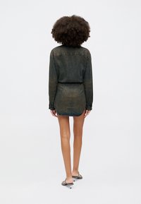 Rochie din denim, de culoare închisă, cu un design subtil decolorat, mâneci lungi și garnitură rotunjită, asortată cu sandale slim.