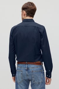 Marineblauw overhemd met lange mouwen en een knoopsluiting, rug yoke en contrasterende knopen. Gecombineerd met lichtblauwe, iets versleten jeans en een geweven bruine riem.
