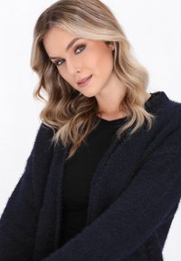 Marineblaues, flauschiges Strickjacke mit weicher Textur, offenem Vorderteil und langen Ärmeln, getragen über einem schwarzen Oberteil.