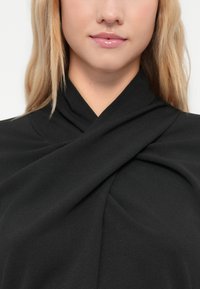 Tuvo plānu uzblīdinātas sievietes ar blondiem matiem, kas valkā spīdīgu rozā lūpu spīdumu un melnu topu ar savītas, sakritušas apkakles