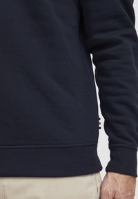 Sudadera de color marino hecha de algodón, con puños y dobladillo en canalé. Etiqueta pequeña con franjas rojas, blancas y azules en el lateral.