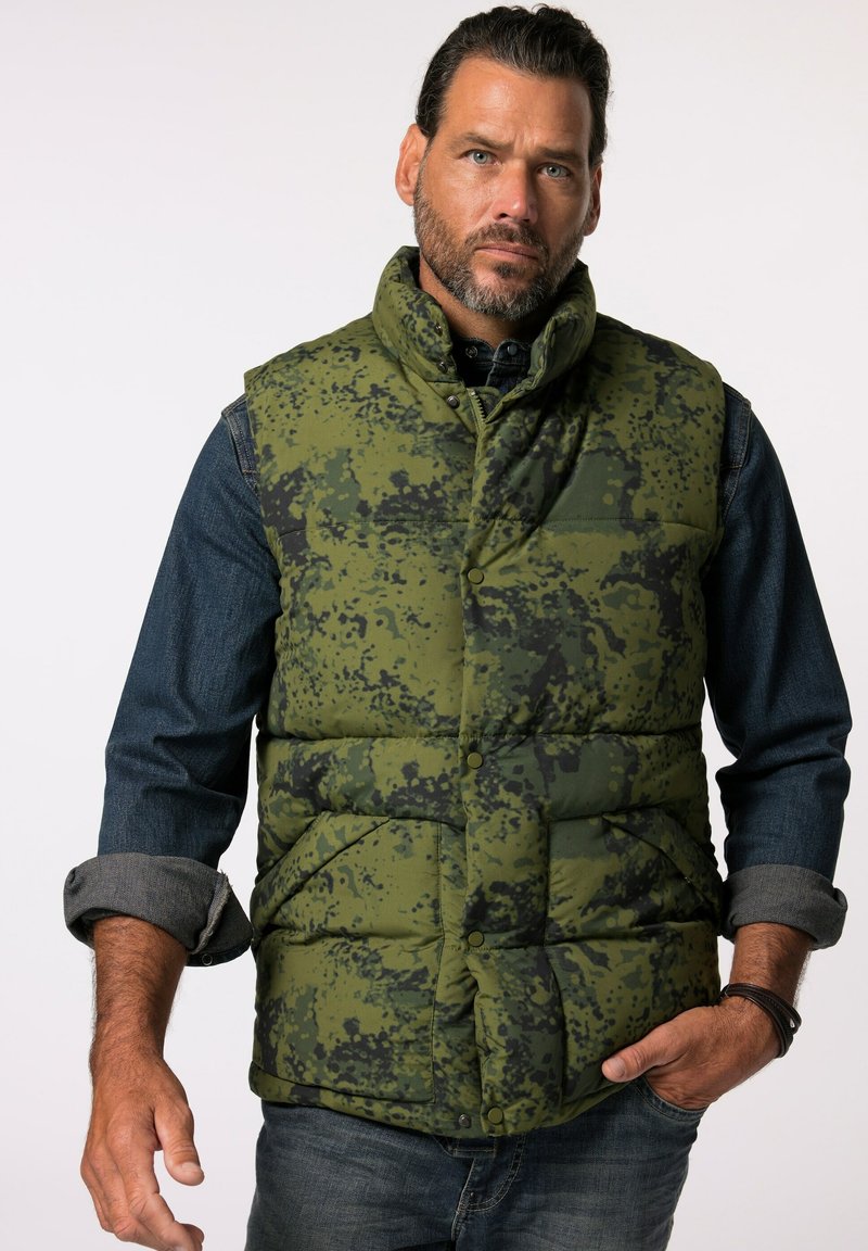 Grüne Camouflage-Steppweste mit hohem Kragen, Druckknopfverschlüssen und zwei Fronttaschen. Getragen über einem Jeanshemd mit hochgekrempelten Ärmeln.