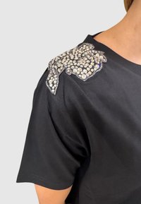 Sort kortærmet t-shirt med en krystalbesat blomsterdesign på venstre skulder. Glat stof med en klassisk pasform.