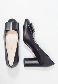 Dei décolleté neri in pelle con tacco alto, punta arrotondata e tacco a blocco alto. Presentano un grande fiocco decorativo e una texture liscia e lucida.