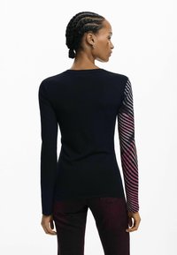 Długi rękaw sweter w kolorze czarnym z teksturą ściąganą; jeden rękaw ma gradientowy wzór w odcieniach różu i czerni. Okrągły dekolt, dopasowany krój.