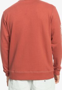 Rostfärgad sweatshirt i mjukt tyg med ribbade ärmslut och fåll. Har en vit logotypdesign på vänster ärm.