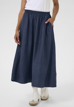 Jupe maxi bleu marine en tissu texturé, avec une taille élastique et des poches latérales, associée à des baskets blanches et des chaussettes moyennes.
