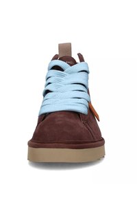 Sneaker in suede marrone con un design di lacci azzurri chiari, dotato di un'etichetta in pelle tan, punta rotonda e suola in gomma beige.