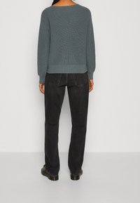 Jasnoniebieski sweter dziany z szerokim dekoltem, prążkowaną fakturą i długimi rękawami, zestawiony z czarnymi, wysokim stanem jeansami i czarnymi butami.