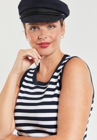 Pasiasty top bez rękawów w kolorze granatowym i białym z okrągłym dekoltem. Noszony z granatową czapką posiadającą pleciony akcent. Gładka dzianinowa tekstura.