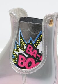 Botte de pluie transparente avec un bout rond, dotée d'un panneau élastique noir et d'un design brodé vibrant en rose, bleu et jaune.