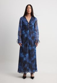 Robe longue et fluide dans des teintes de bleu avec un motif tie-dye, décolleté en V profond, détail central froncé et manches ajustables à nouer.