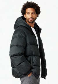 Doudoune noire avec capuche, fermeture zippée et poignets élastiques. Le matériau présente une texture lisse et brillante avec des détails de coutures horizontales.