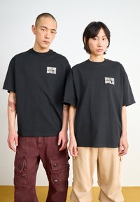 Black cotton t-shirts with a small white graphic on the chest, paired with contrasting cargo pants in maroon and beige.