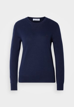 Mörkblå stickad tröja med rund halsringning. Har långa ärmar och ribbat nederkant. Lacoste-logotyp i matchande färg på bröstet.